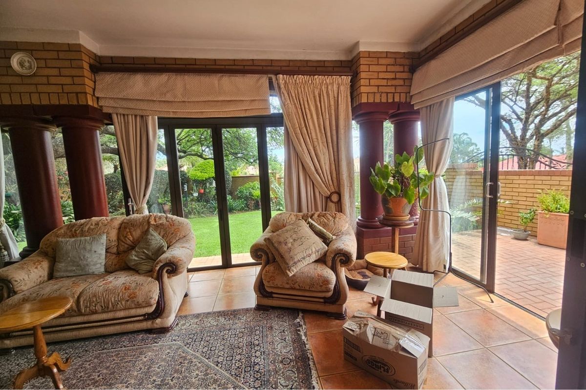 Spacious living room featuring ceramic tile flooring, prominent brick columns, and large sliding glass doors providing direct access to the garden and patio area.
