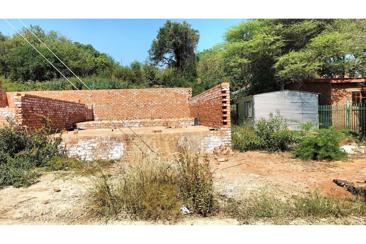 Vacant residential land featuring an unfinished brick structure foundation and a small corrugated metal storage shed on the property.