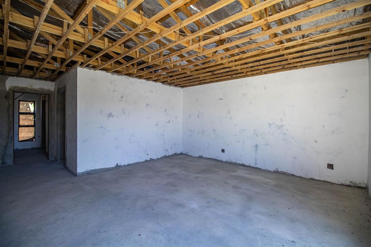 An unfinished interior room featuring exposed timber roof trusses, raw concrete flooring, and unpainted plaster walls, offering a blank canvas for renovation.