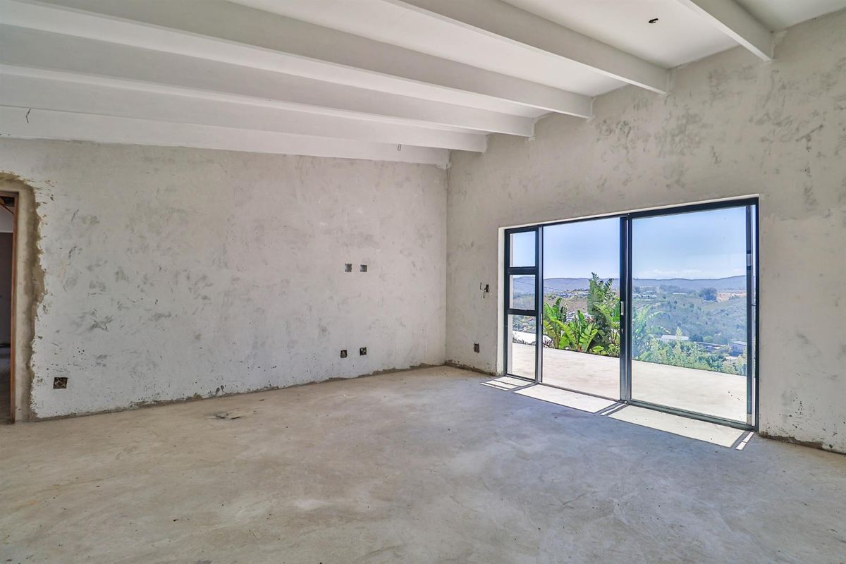 An unfinished living area featuring exposed concrete floors, raw plastered walls, exposed ceiling beams, and large sliding glass doors opening to a scenic view.
