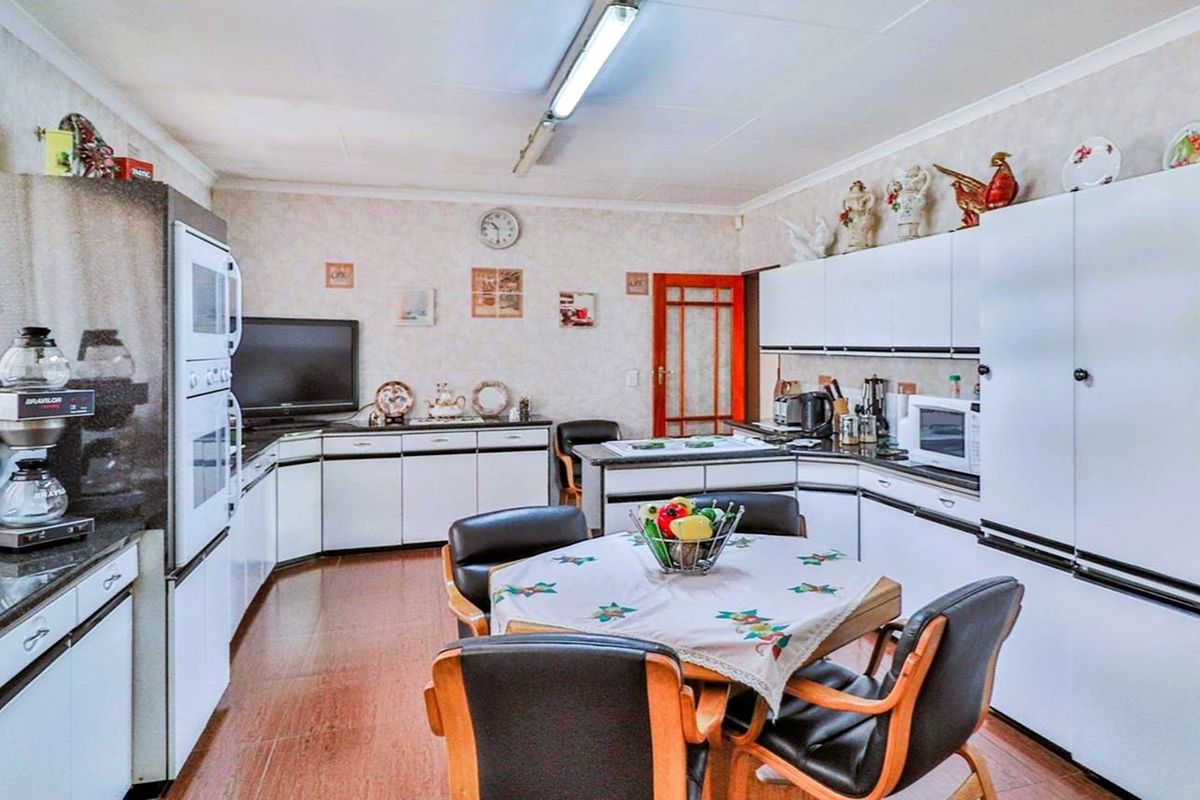 A functional kitchen featuring white cabinetry, dark countertops, built-in oven, and a central dining area with wood-look flooring.