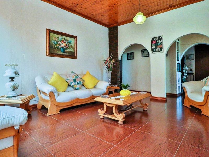 A living room featuring tiled flooring, a timber-clad ceiling, and arched doorways leading to adjacent spaces.