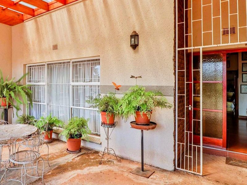 A covered patio area featuring a timber pergola, security gate, and large windows, providing a functional outdoor space for relaxation.