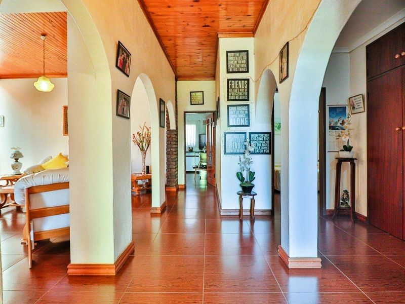 A spacious hallway featuring arched architectural openings, tiled flooring, and a timber-paneled ceiling, providing access to adjacent living areas.
