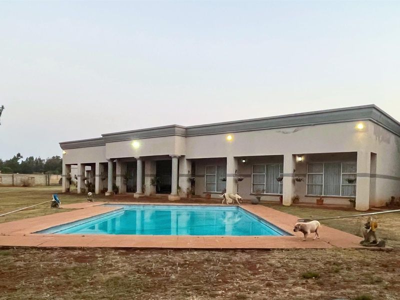 Rear view of the house featuring a swimming pool, covered patio area with columns, and a large surrounding garden.