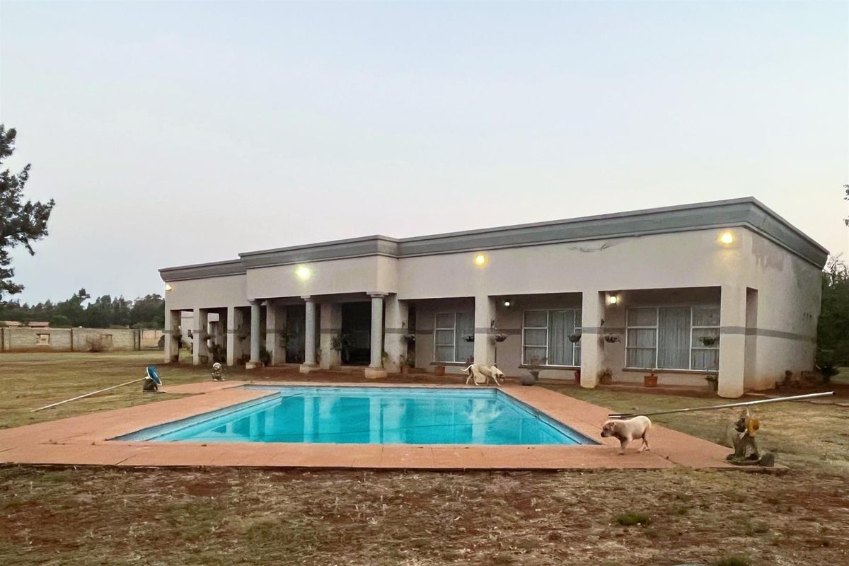 Rear view of the house featuring a swimming pool, covered patio area with columns, and a large surrounding garden.