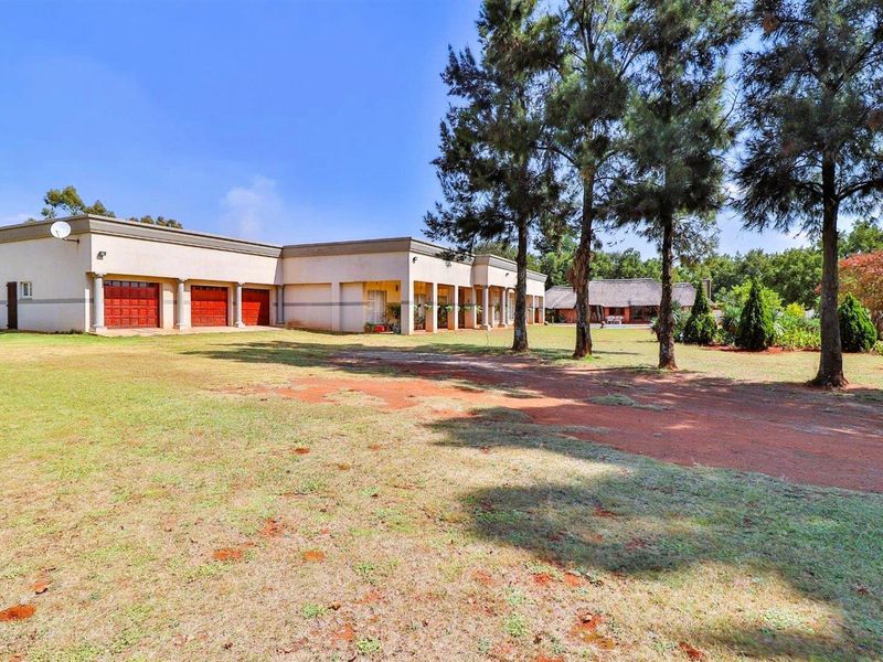 Spacious exterior view of the property featuring a multi-car garage, covered patio area, and expansive surrounding grounds with mature trees.