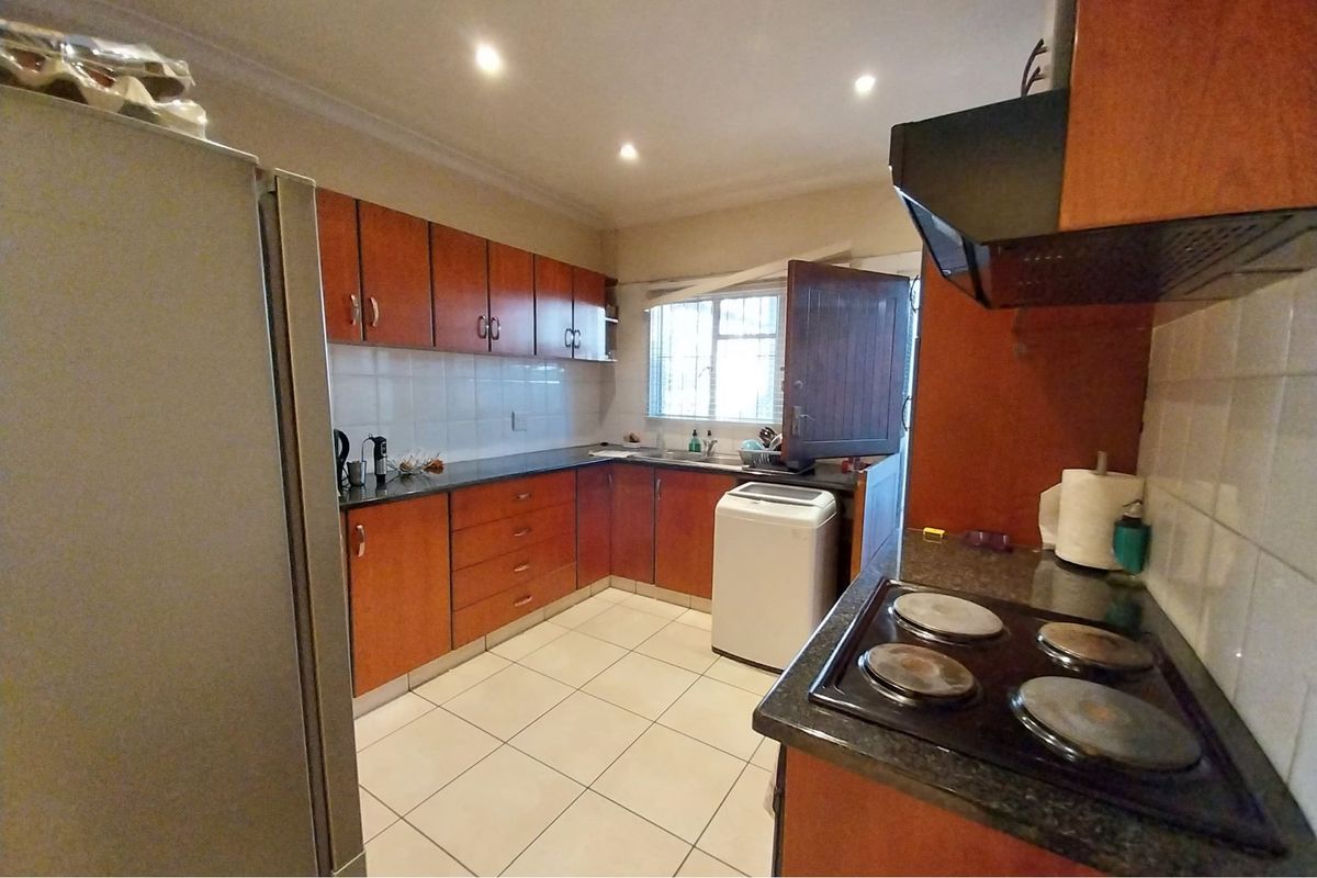 Functional kitchen featuring wooden cabinetry, granite countertops, electric hob, extractor fan, and tiled flooring with direct access to an exterior door.