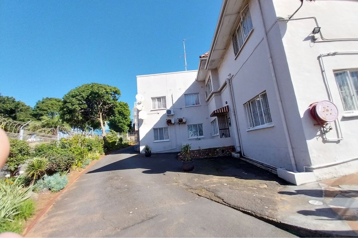 Rear exterior view of the apartment building featuring an asphalt driveway, external air conditioning units, and a fire hose reel.