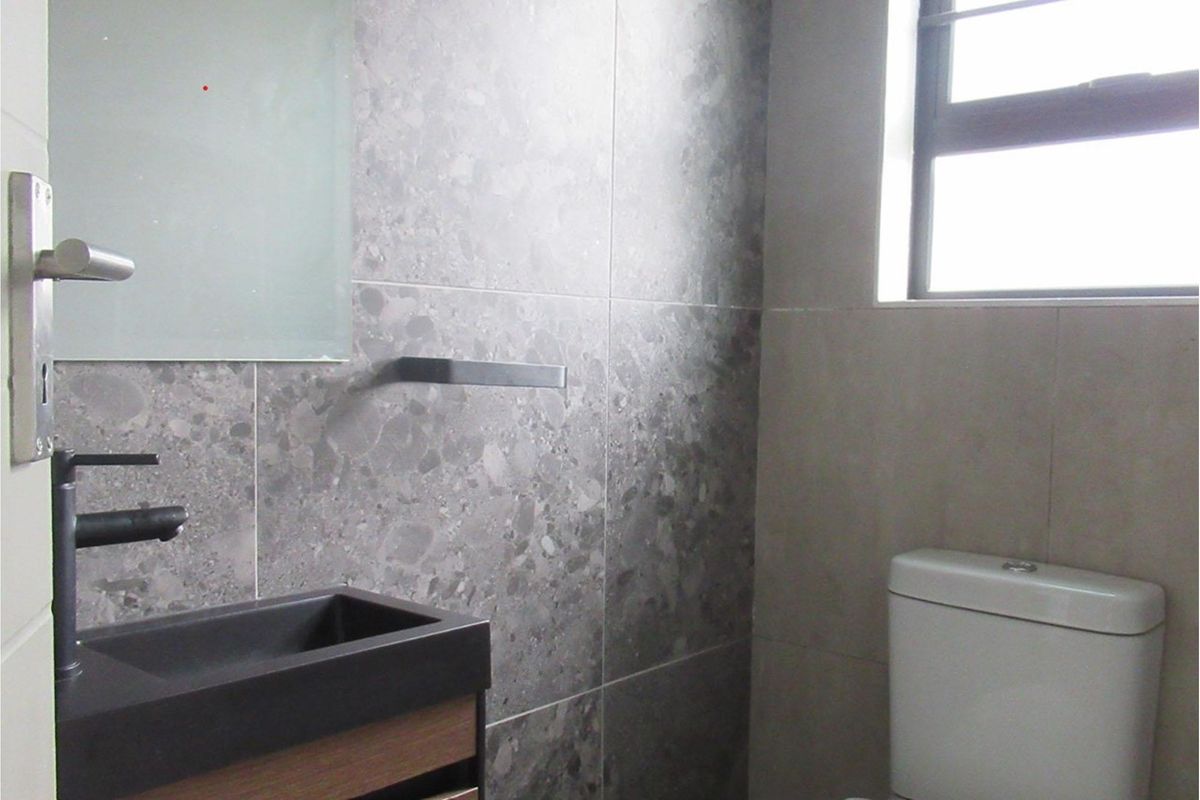 Modern bathroom featuring grey stone-look wall tiles, a contemporary vanity with a dark basin, and a white toilet.