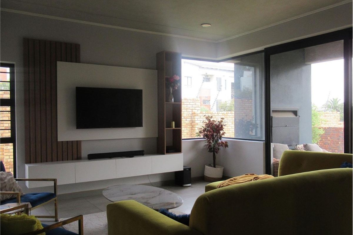 Modern living room featuring a built-in media wall with timber slat detailing, sleek cabinetry, and large corner windows providing natural light and garden views.