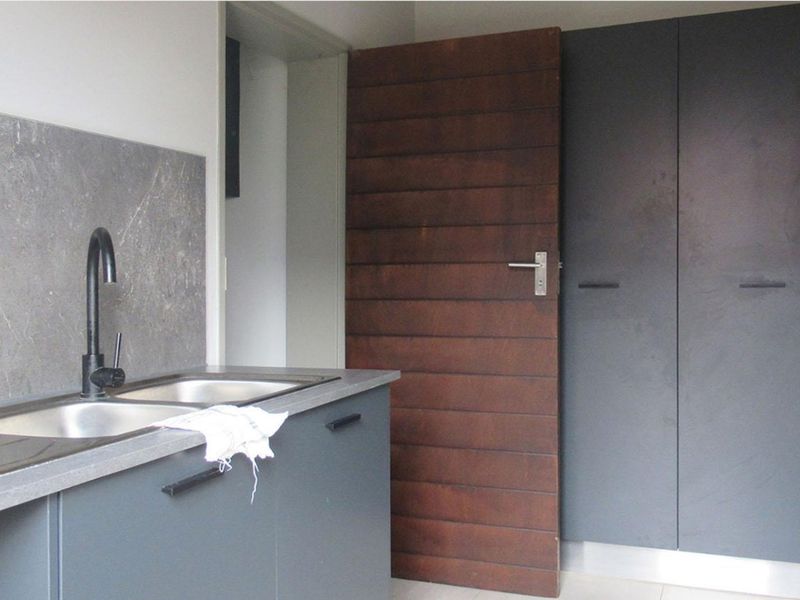 A functional scullery area featuring dark cabinetry, a stainless steel double sink with a modern black faucet, and a stone-look splashback.