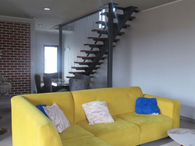 Open plan living area featuring a modern floating staircase with metal stringers and cable balustrades, complemented by a decorative brick feature wall.