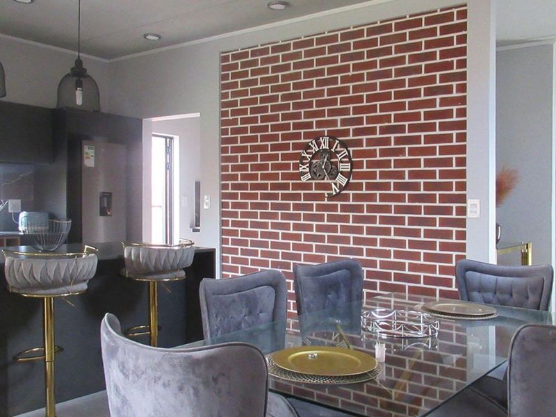Open plan living and dining area featuring a modern kitchen with dark cabinetry and a decorative exposed brick feature wall.