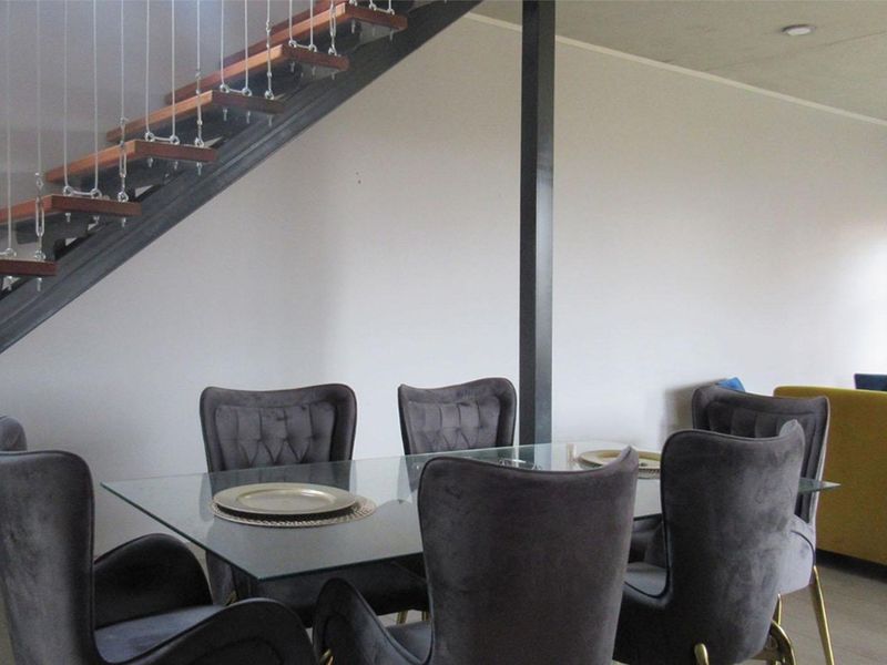 A dining area featuring a modern floating staircase with timber treads and steel cable balustrades, set against a neutral interior backdrop.