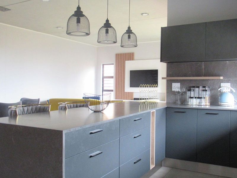 Modern open-plan kitchen featuring dark matte cabinetry, stone countertops, and stylish pendant lighting, seamlessly flowing into the adjacent living area.