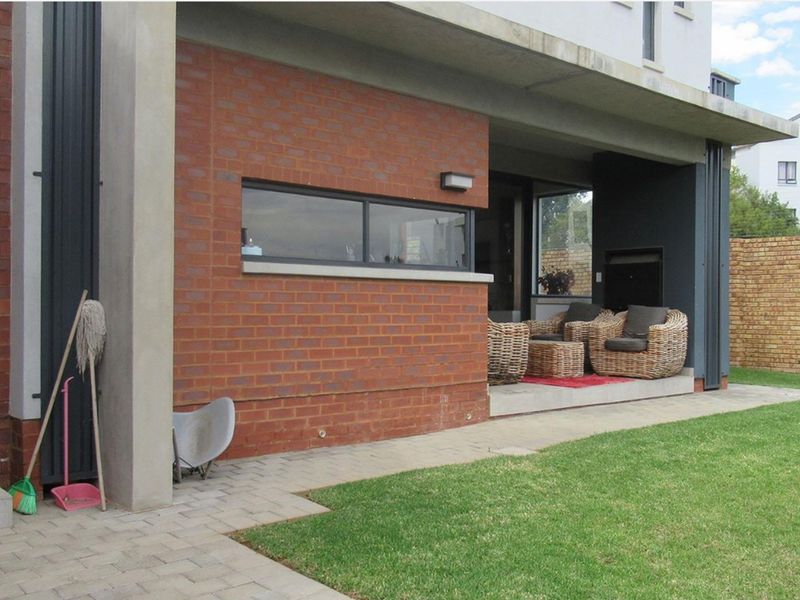 A covered patio area featuring a built-in fireplace, brick facade, and concrete flooring, overlooking a well-maintained garden.