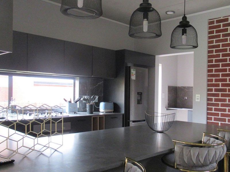 Modern kitchen featuring dark cabinetry, a spacious island, integrated appliances, and a distinctive brick feature wall, with an adjacent scullery area.