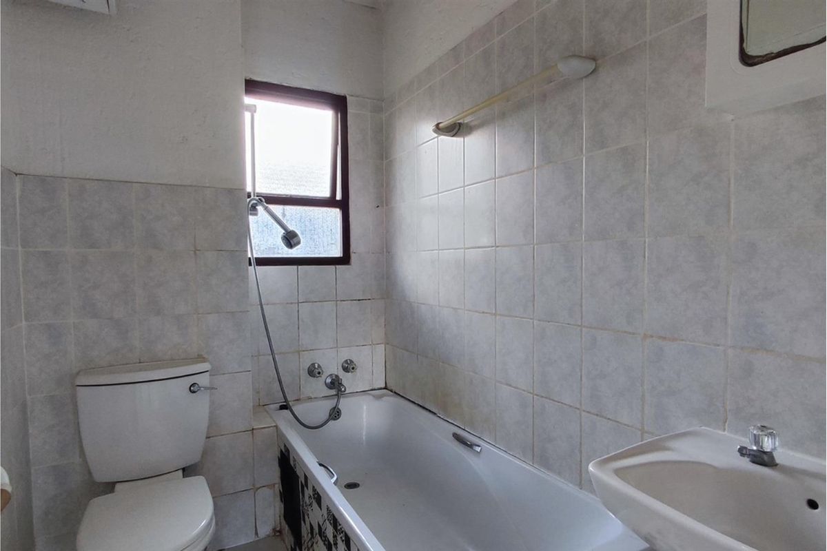 A dated bathroom featuring a standard bathtub with shower attachment, a toilet, and a wall-mounted basin with tiled walls.