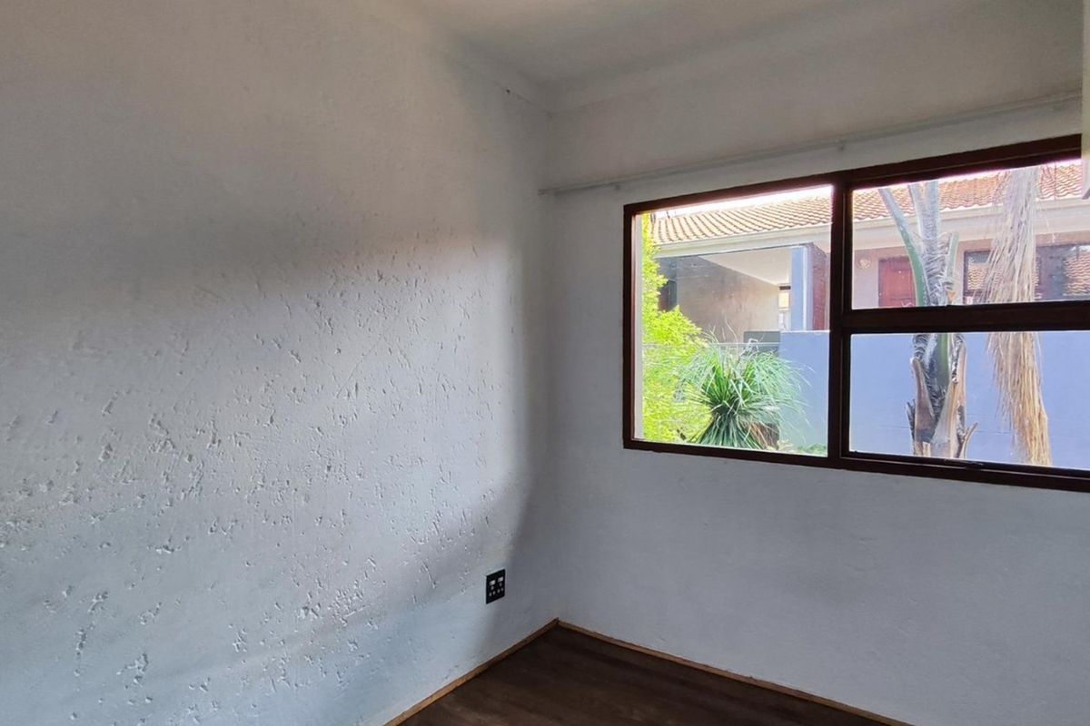 A bright, empty bedroom featuring dark wood-look flooring, textured walls, and a window overlooking the exterior area.