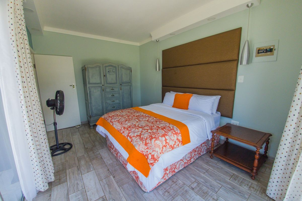 A well-maintained bedroom featuring wood-look tile flooring, a large upholstered headboard, and modern pendant lighting.