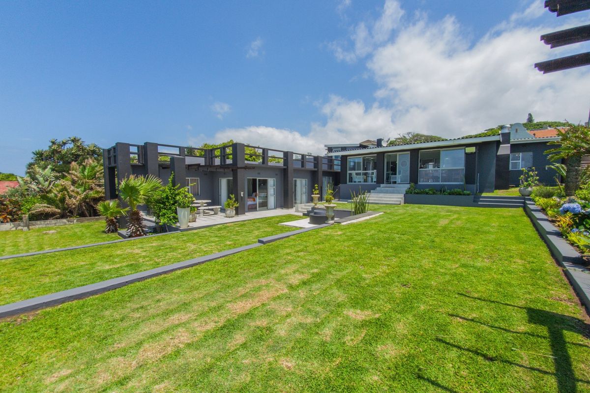Rear view of a modern house featuring a spacious lawn, landscaped garden, and a large terrace with sliding glass doors providing indoor-outdoor flow.
