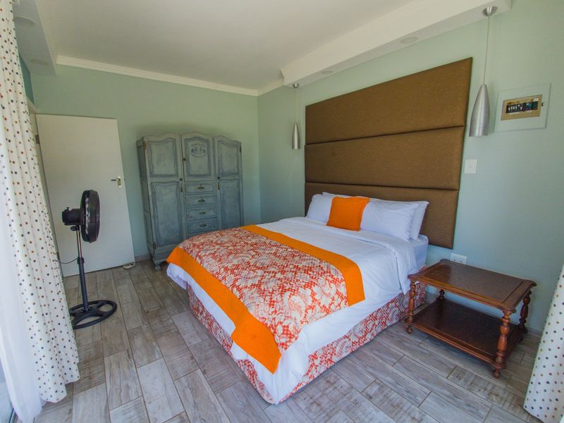 A well-maintained bedroom featuring wood-look tile flooring, a large upholstered headboard, and modern pendant lighting.