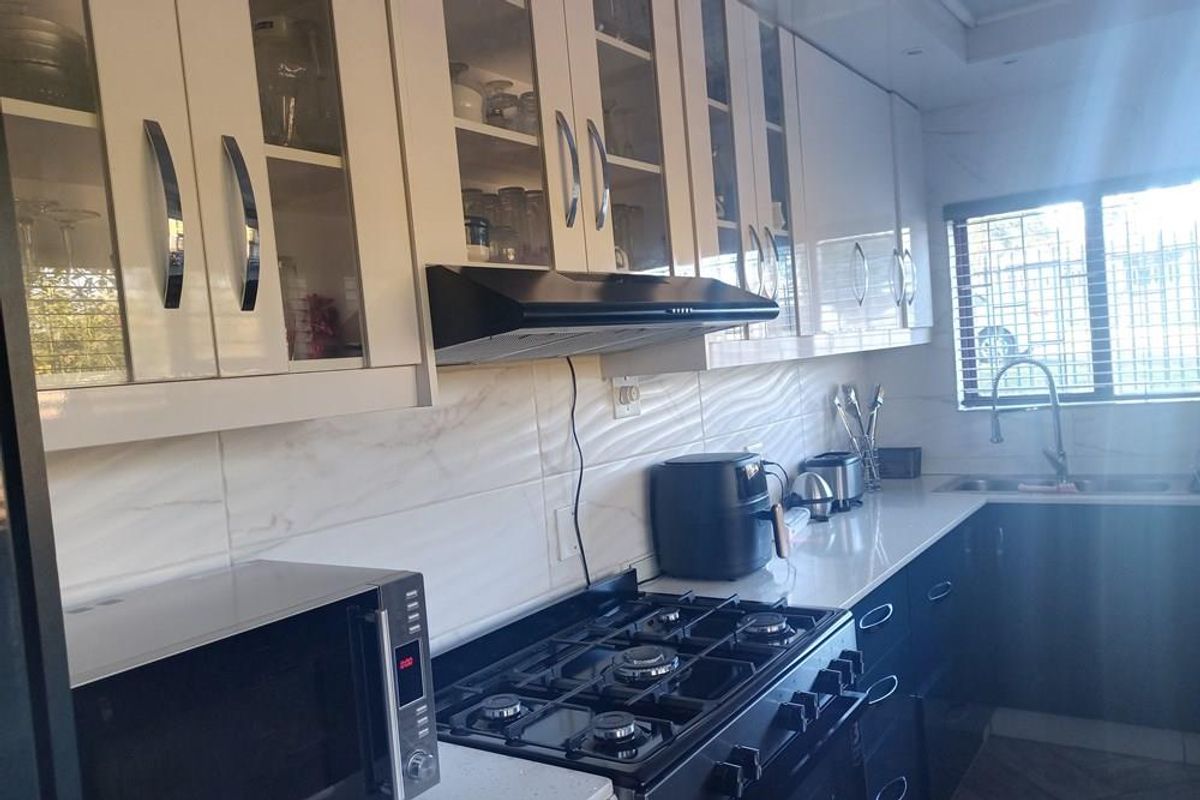 Modern kitchen featuring white high-gloss cabinetry, stone countertops, a gas hob with extractor fan, and a stainless steel sink with a modern faucet.