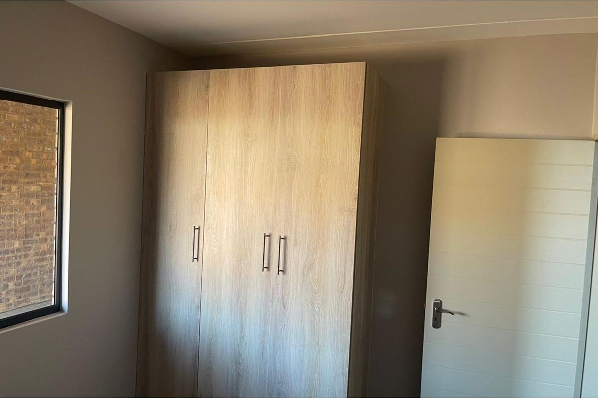A bedroom featuring a built-in wooden wardrobe with modern handles and a neutral color palette.