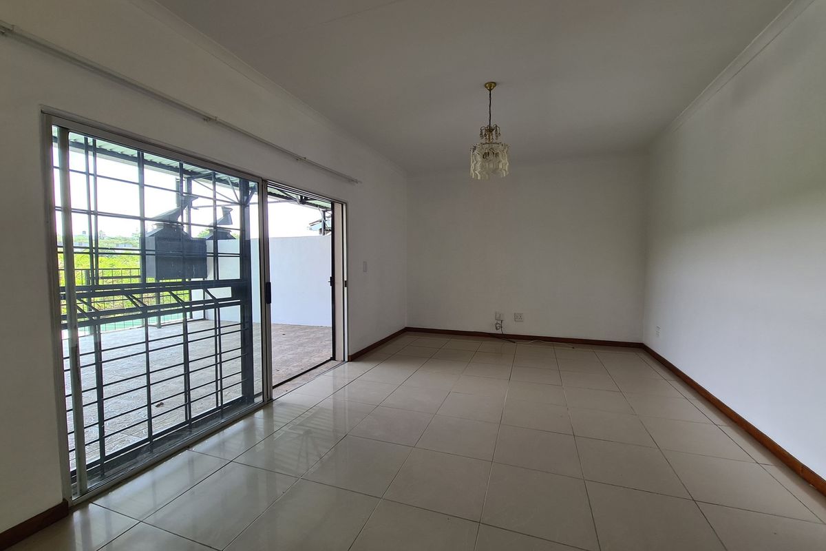 Spacious living area featuring neutral floor tiles, a decorative light fixture, and large sliding glass doors providing direct access to an outdoor patio.
