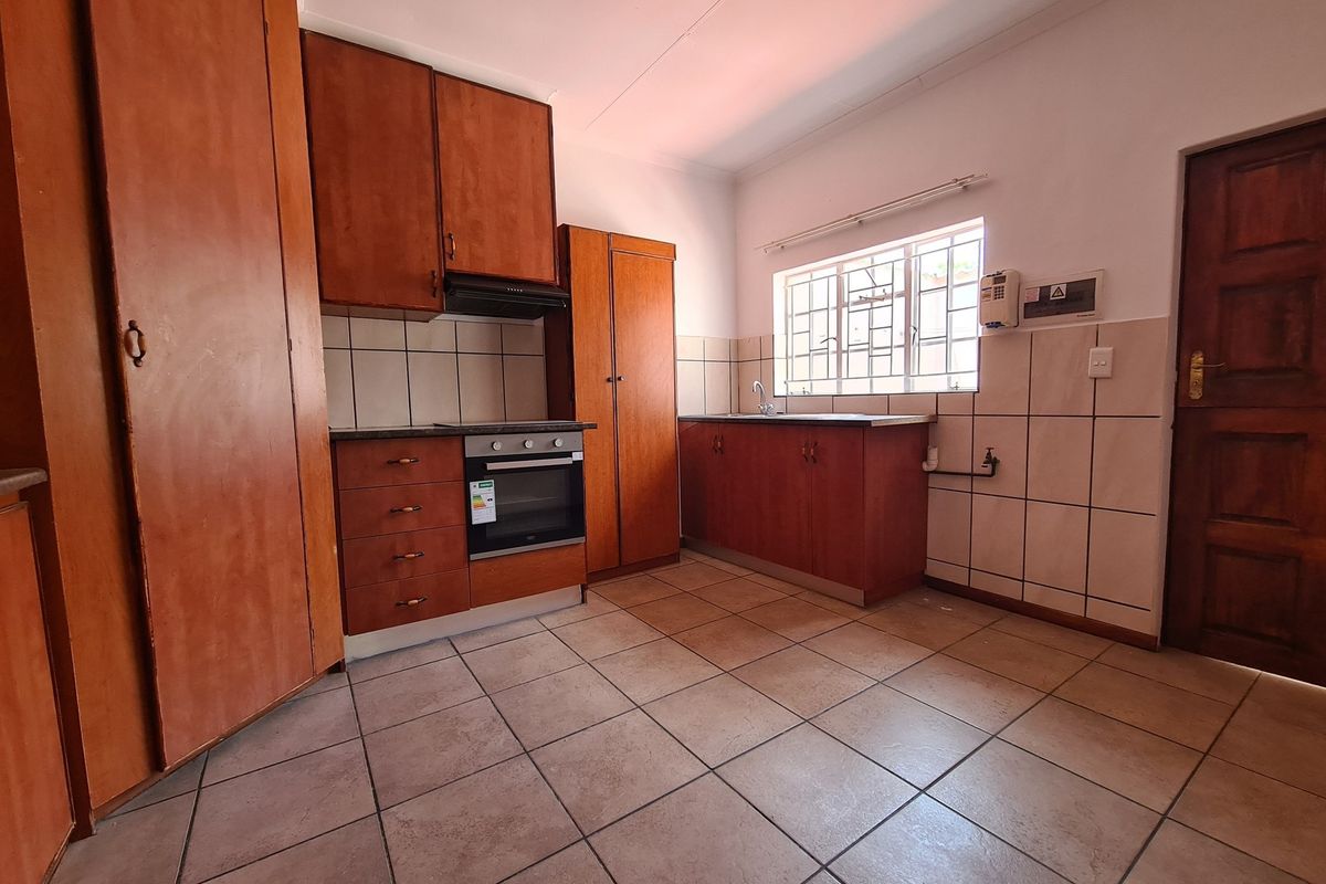 A functional kitchen featuring wooden cabinetry, built-in oven, extractor fan, tiled flooring, and a window with security bars.