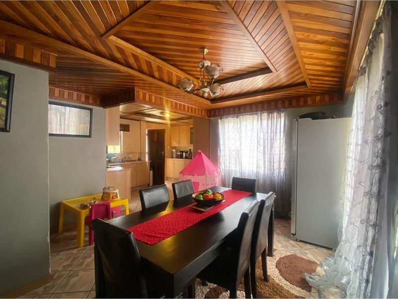 Open plan dining area featuring a distinctive wooden panelled ceiling, tiled flooring, and seamless flow into the adjacent kitchen space.