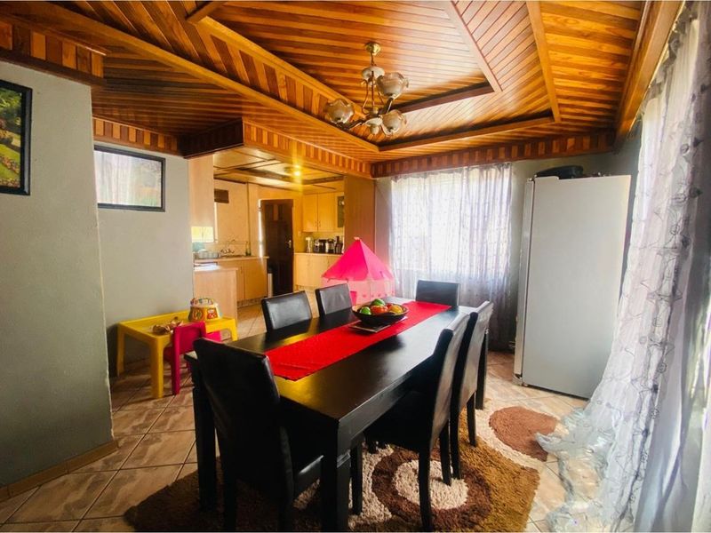 Open plan dining area featuring a distinctive wood-paneled tray ceiling, tiled flooring, and an adjacent kitchen space.