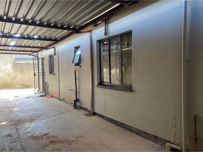 A covered outdoor patio area featuring a concrete floor, corrugated metal roof, and exterior wall access with security bars on windows.