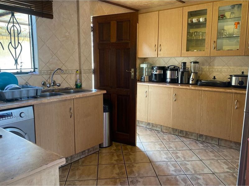 A functional kitchen featuring light wood cabinetry, tiled flooring, tiled splashbacks, and a double sink with integrated laundry appliance space.