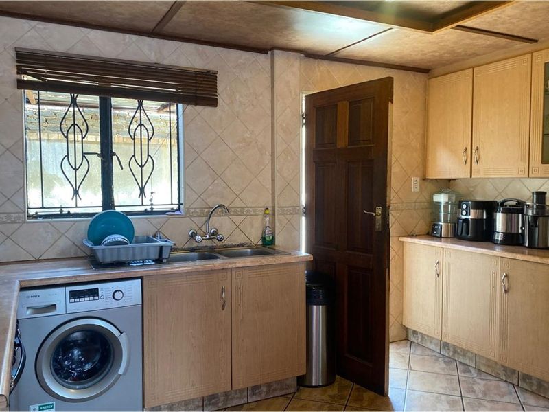 A functional kitchen featuring light wood cabinetry, tiled walls, a double sink, and an integrated washing machine with direct outdoor access.