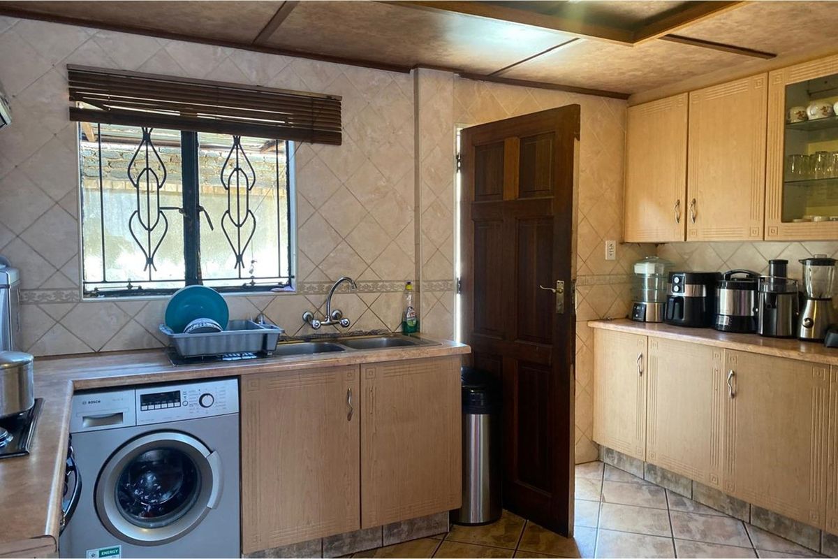 A functional kitchen featuring light wood cabinetry, tiled walls, a double sink, and an integrated washing machine with direct outdoor access.