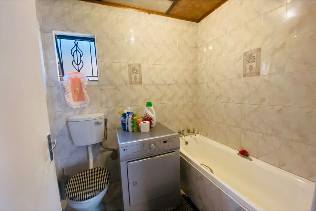 A compact bathroom featuring a standard bathtub, toilet, and space for a laundry appliance, finished with dated wall tiles.