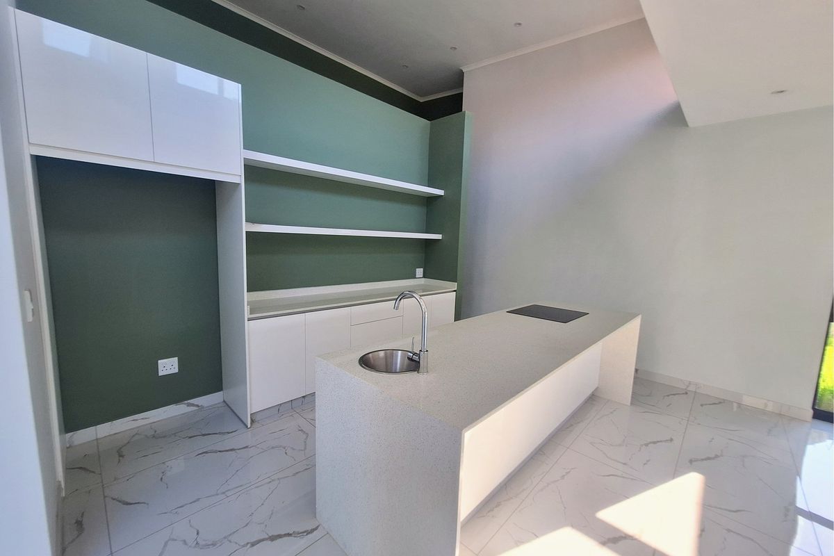 Modern kitchen featuring a central island with a built-in sink and cooktop, complemented by sleek white cabinetry and open shelving against a green accent wall.