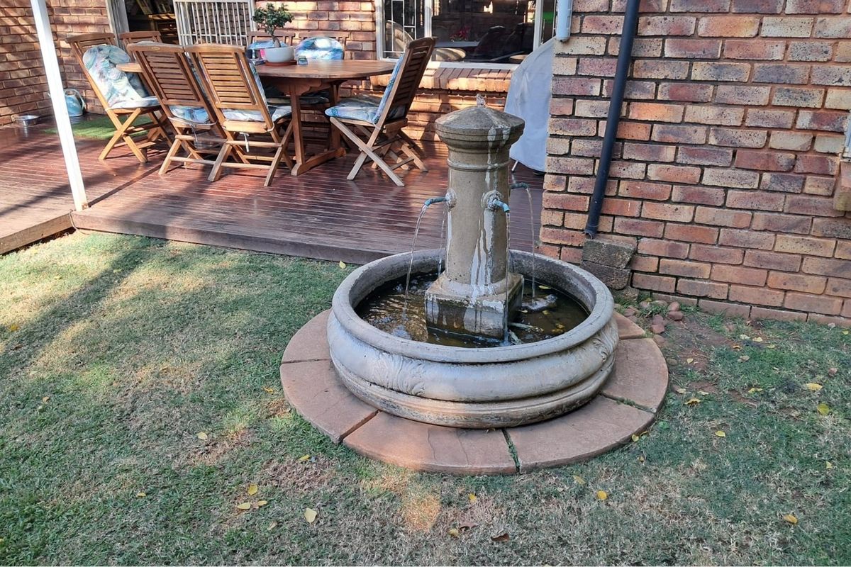 A rear garden area featuring a stone water fountain, brick exterior wall, and a timber deck patio space.
