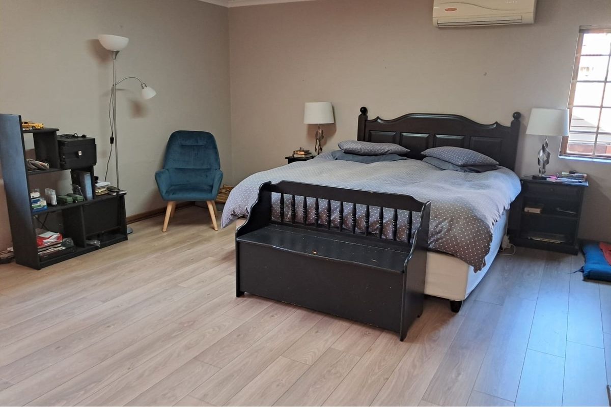 A spacious bedroom featuring light-toned laminate flooring and a wall-mounted split-system air conditioning unit.