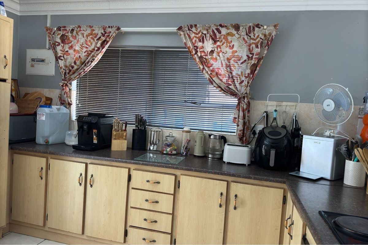 A functional kitchen area featuring light wood-finish cabinetry, dark laminate countertops, and a window with fitted blinds.