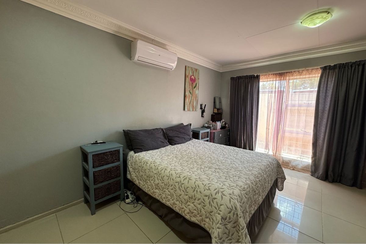 A bedroom featuring tiled flooring, crown molding, and a wall-mounted air conditioning unit, with sliding door access to the exterior.
