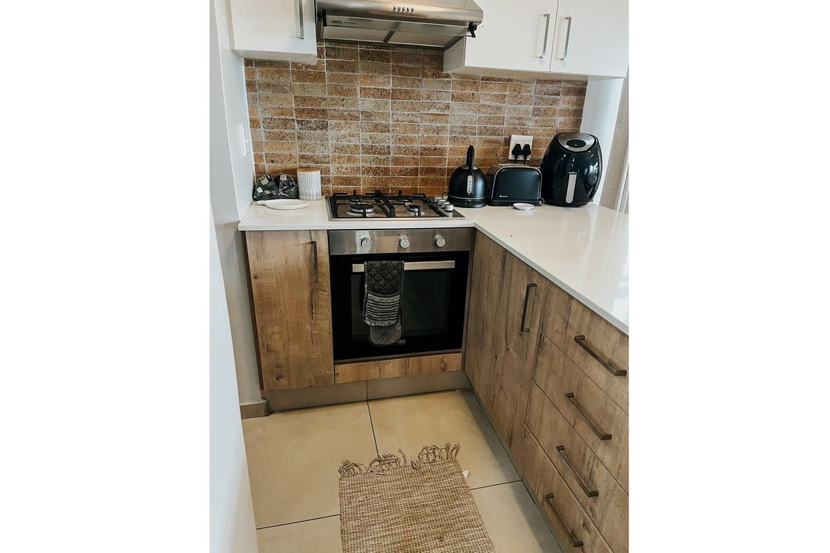 Compact kitchen featuring wood-look cabinetry, stone countertops, a gas hob, built-in oven, and a textured tile backsplash.