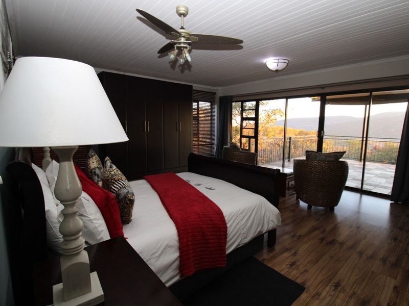 Spacious bedroom featuring wood-look flooring, built-in cupboards, a ceiling fan, and large sliding glass doors opening onto a private balcony with scenic views.