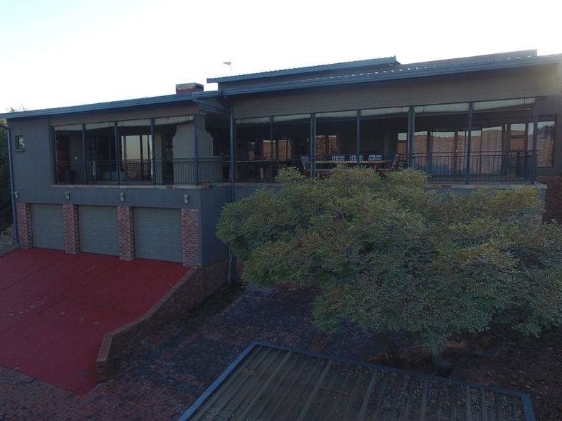 An elevated view of the rear exterior of the house, featuring a large covered patio, triple garage, and paved driveway area.