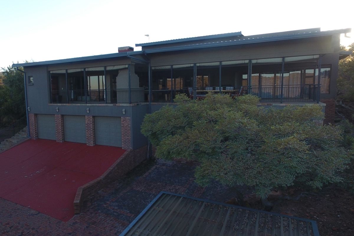 An elevated view of the rear exterior of the house, featuring a large covered patio, triple garage, and paved driveway area.