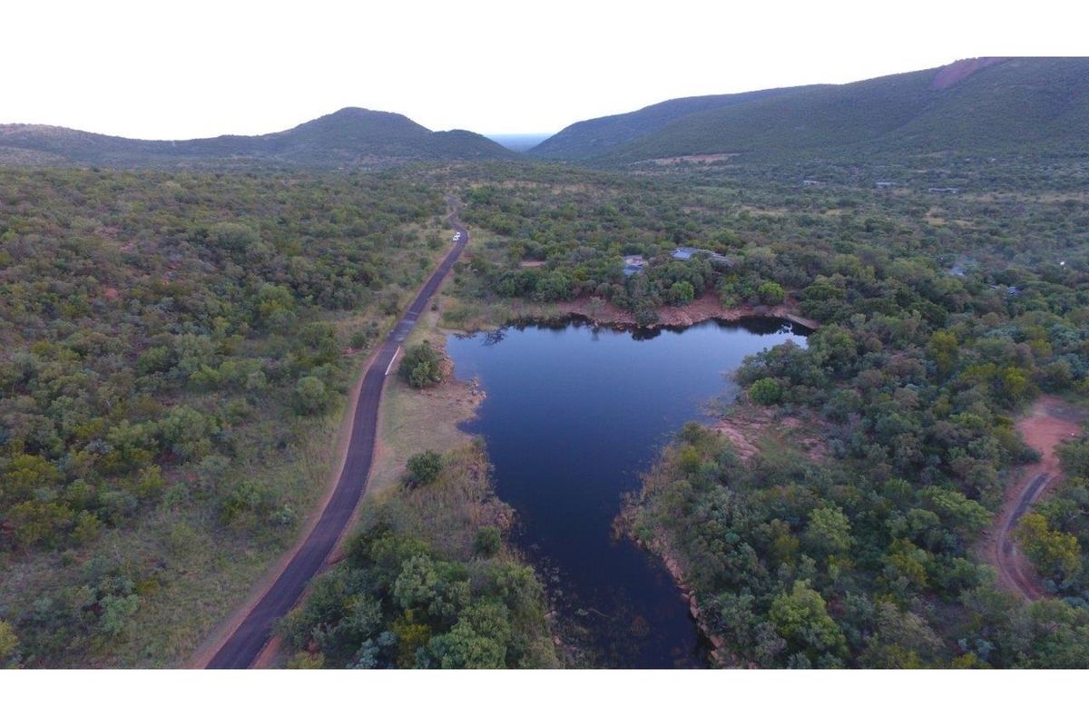 An aerial view of the property landscape, featuring a natural dam, surrounding indigenous bushveld, and access roads within a scenic mountainous estate.