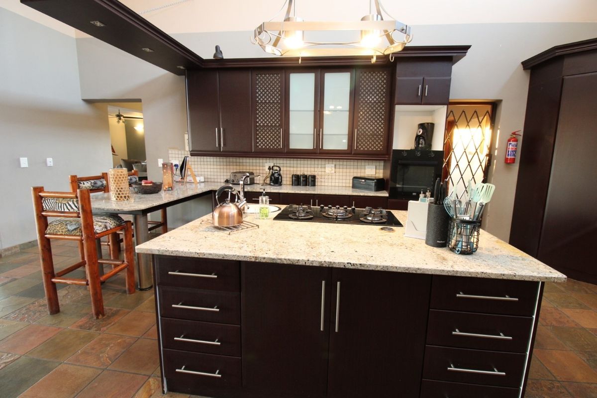 Spacious kitchen featuring dark wood cabinetry, granite countertops, a central island with a built-in gas hob, and tiled flooring.