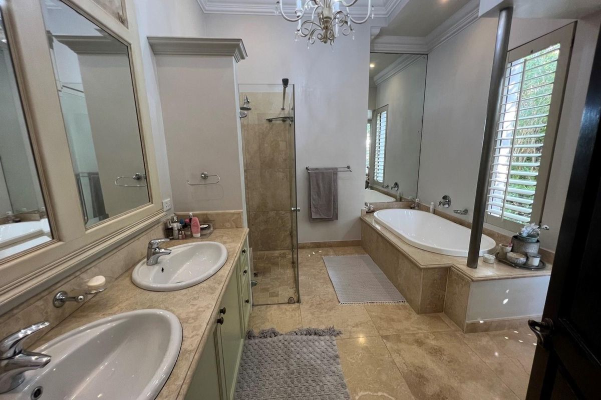 A well-appointed bathroom featuring a double vanity with stone countertops, a built-in bathtub, and a separate glass-enclosed shower with tiled finishes.